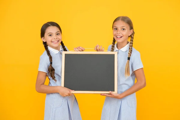 Σχολικά νέα. Αληθινές πληροφορίες. Τα μικρά κορίτσια κρατούν το γράψιμο της επιφάνειας κίτρινο φόντο. Κενή πλακέτα για πληροφορίες. Φρέσκος χώρος αντιγραφής πληροφοριών σχολείου. Παιδιά και πίνακας για τη συγγραφή πληροφοριών — Φωτογραφία Αρχείου
