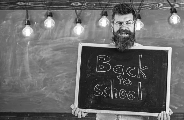 Homme avec barbe et moustache sur le visage heureux accueille ses collègues, tableau sur fond. Professeur de lunettes tient tableau noir avec titre de retour à l'école. Embauche enseignants concéder — Photo