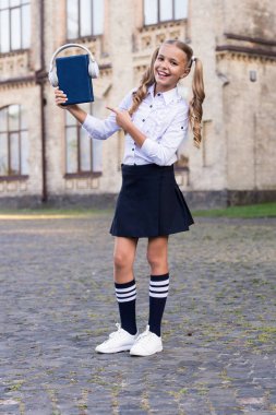 Dinleme okul kitabı. Bilgi bu şekilde daha iyi asimile. Sesli kitap konsepti. Öğrenme için dijital teknolojiler. E-öğrenme ve modern yöntemler. Kız sevimli kız öğrenci kitap ve kulaklık tutun