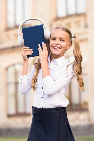 E-learning és modern módszerek. Girl aranyos iskoláslány Hold könyv és fejhallgató. Tudás elsajátítani jobb így. Hangoskönyv koncepció. Hallgató iskolai könyv. Digitális tanulási technológiák — Stock Fotó