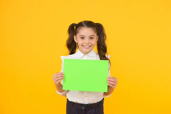 Voici vos devoirs. Adorable petit enfant tenant une feuille de devoirs vide sur fond jaune. Jolie petite fille avec le papier vert vierge de l'école pour faire devoir. Travail à domicile, espace de copie — Photo