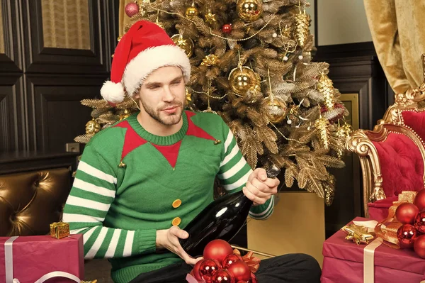 El hombre celebra la fiesta de año nuevo. Santa hombre abre la botella de champán en el árbol de Navidad. La fiesta está cerca, da una gran alegría. Tener un nuevo año simplemente hermoso — Foto de Stock
