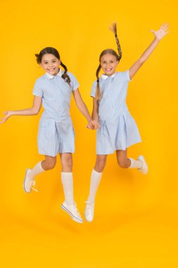 Eğleniyorum. Eski moda. Klasik tarzda çocuklar. Eski usul. Mutlu arkadaşlar sarı arka planda zıplarlar. Çocuk modası güzeli. çocukluk mutluluğu. Kardeşlik kavramı. Okul üniformalı küçük kızlar