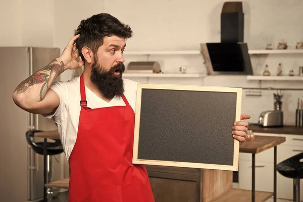 Qué cocinar. Sorpresa. Esto es lo que necesitas. Hipster en la cocina. Menú de restaurante o cafetería. Anuncio. Hombre barbudo con delantal rojo. Hombre maduro. Cocinero barbudo. Hombre chef con tabla, espacio de copia —  Fotos de Stock