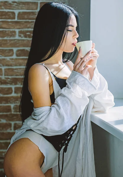 Sensual girl sexy breasts drinking coffee near windowsill. Attractive female lingerie relaxing at home. Passionate mysterious lover. Perfect coffee time. But first coffee. Enjoying morning sunlight — Stock Photo, Image