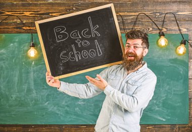 Gözlüklü öğretmen okula geri başlık ile tahta tutar. Mutlu yüzünde sakallı ve bıyıklı adam öğrencileri, arka planda tebeşir tahtasıyla karşılıyor. Lise concep