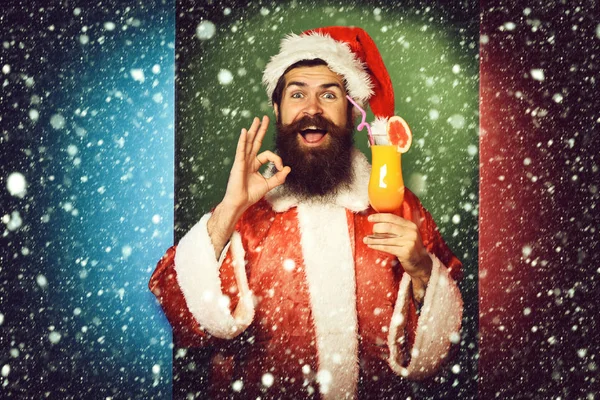 renkli stüdyo backgroun ok gösteren noel veya xmas kazak ve yeni yıl şapka alkolsüz kokteyl cam tutan gülümseyen yüzünde uzun sakallı yakışıklı sakallı noel baba adam