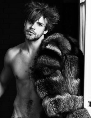 Sexy macho tousled hair coming out bedroom door. Richness and luxury concept. Bachelor rich lover. Guy attractive posing fur coat on naked body. Luxury lifestyle and wellbeing. Luxury status symbol clipart
