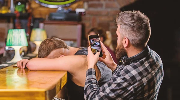 Hombre borracho duerme y chico con smartphone. Hipster tomando fotos borracho amigo. Amigos borrachos en el bar. Duerme en el mostrador del bar. Toma una foto para recordar la fiesta. Hipster burlándose de amigo borracho —  Fotos de Stock