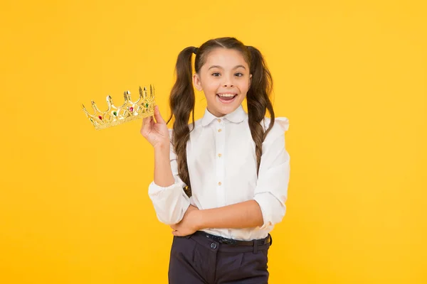 彼女の誇りだ。黄色の背景に誇りを持って王冠を保持幸せな小さな女の子。愛らしい小さな学校の美しさの女王笑顔と偉大な誇りを感じています。それは彼女の誇りの問題 — ストック写真