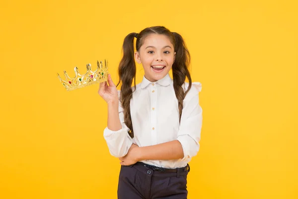 Ese orgullo suyo. Niña feliz sosteniendo la corona con orgullo sobre fondo amarillo. Adorable pequeña reina de belleza de la escuela sonriendo y sintiendo gran orgullo. Es una cuestión de orgullo. — Foto de Stock