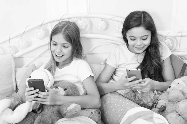 New technology. Happy little children with mobile phone. Ordering gifts for Christmas and New Year by phone. Little girls use smartphone in bed. Merry Christmas and Happy New Year greetings