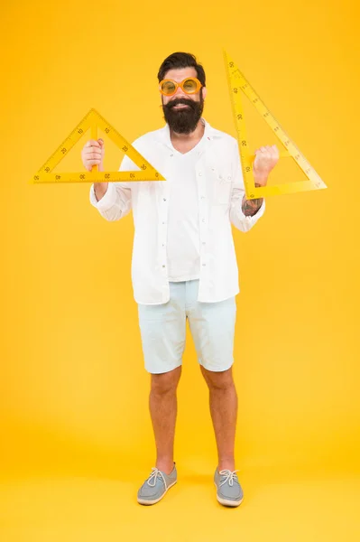 Тут легко вивчити трикутники. Щасливий бородатий чоловік тримає трикутники на жовтому тлі. Шкільний вчитель або студент посміхається з геометричними трикутниками для уроку геометрії. Урок у трикутниках — стокове фото