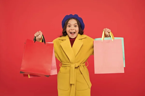 Obtener descuento de compras en vacaciones de cumpleaños. Fashionista adoro ir de compras. Satisfacción del cliente Prima vez comprar ropa de primavera. Obsesionado con las compras. Chica lindo niño mantenga bolsas de compras fondo rojo — Foto de Stock