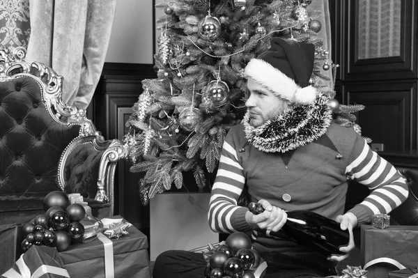 Champagne et le plaisir continue. Homme au chapeau de Père Noël tenir de nouveaux cadeaux de l'année. Joyeux Noël et bonne année. Homme heureux avec de nouvelles boîtes-cadeaux de l'année. Guy fête le nouvel an à la maison — Photo