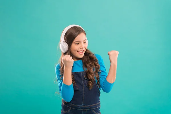 No es más que una ganadora. Niño feliz haciendo gesto ganador sobre fondo azul. Pequeño ganador escuchando música en auriculares. Emocionado ganador o campeón celebrando la victoria — Foto de Stock