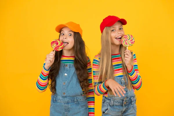 Lekker likken. Kleine meisjes genieten van heerlijke smaak van lolly 's op gele achtergrond. Kleine kinderen likken snoepjes met een klassieke fruitsmaak. Het smaakt zo lekker. Zoete smaak van de jeugd — Stockfoto