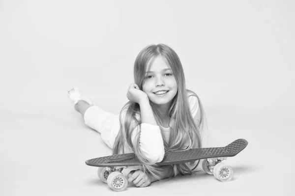 Extrémní dítě. Malé dítě se uklidňuje na skateboard na růžovém pozadí. Roztomilé malé dítě s fialovou penzí. Rozkošná holka s bruslačem a vypadat — Stock fotografie