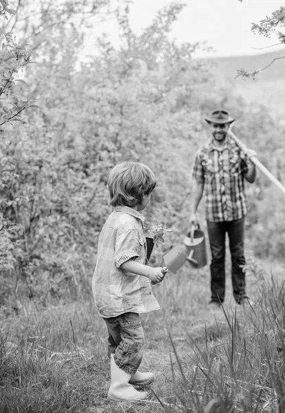 Маленький мальчик помогает отцу в сельском хозяйстве. Счастливого Дня Земли. Питомник семейного дерева. поливальная банка, кастрюля и мотыга. Садовое оборудование. Эко-ферма. отец и сын в ковбойской шляпе и резиновых сапогах на ранчо — стоковое фото