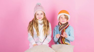 Stay warm and comfortable. Warm up your winter wear with cute and cozy accessories. Siblings wear winter warm hats sit on pink background. Children boy and girl warm up with pillows and hats