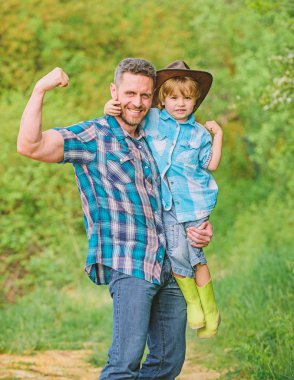 Çiftlikteki kovboy şapkalı güçlü baba ve oğul. Lastik çizmeli çocuk. Ormanda mutlu bir baba. İnsan ve doğa. Aile günü. Dünya günün kutlu olsun. Eko çiftliği. Küçük çocuk çiftçilikte babasına yardım ediyor. güçlü bağlar