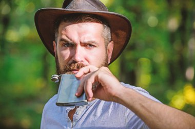 Vahşi batıyı ısıtıyor. Bahar güneşli hava. kamp ve yürüyüş. acımasız bakmak ile olgun erkek şişeden alkol içmek. Açık havada kovboy şapkalı sakallı adam. sonbahar ormanda adam hipster