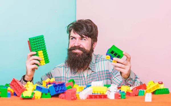 Still child in his soul. Man bearded hipster play plastic bricks. Create construction blocks. Colorful details. Build constructions. Guy happy face play constructor. Create funny constructions