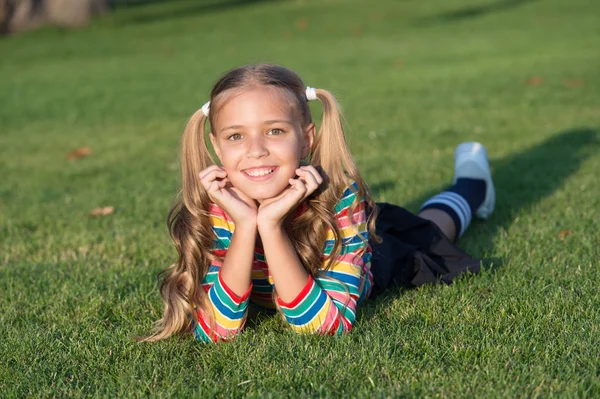Living happy life. Have fun. Girl kid laying green grass. Healthy emotional happy kid relaxing outdoors. Girl ponytails hairstyle enjoy relax. Cheerful schoolgirl on sunny day. Happy smiling pupil