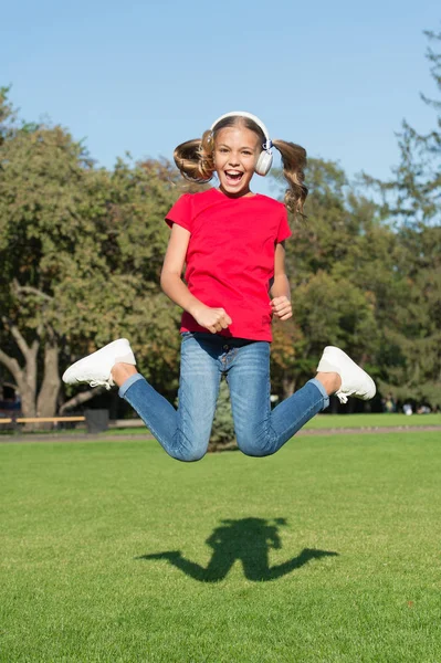 Stereo kulaklıklar. Modern teknolojiyi kullanan bir çocuk. Modern çocuk. Mükemmel yüksek ses. Hiç bitmeyen neşe. Kız müzik modern gadget dinleme. Çocuk kablosuz kulaklık dans atlama ile mutlu