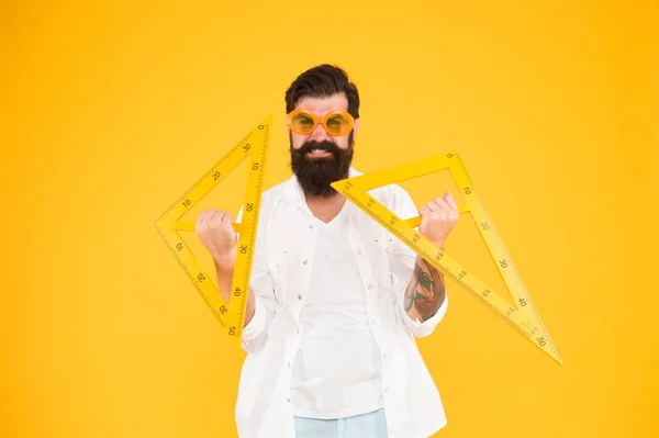 La educación superior comienza aquí. Profesor universitario sosteniendo triángulos sobre fondo amarillo. Hombre barbudo preparándose para estudios universitarios. Universidad de ingeniería. Tu educación, tu universidad — Foto de Stock