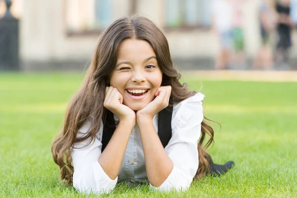 Winking to you. School break for rest. Adorable pupil. Girl kid laying lawn. Girl school uniform enjoy relax. Importance of relaxation. Little schoolgirl. Relax at school yard. Kid relaxing outdoors