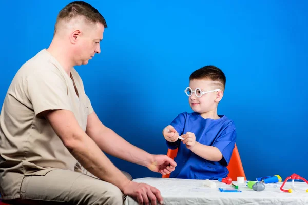 Niño lindo niño y su padre médico. Trabajador del hospital. Concepto de medicina. El pequeño doctor se sienta en la mesa de herramientas médicas. Tratamiento de enfermedades. Papá y su hijo dinastía médica. Salud. Examen médico — Foto de Stock