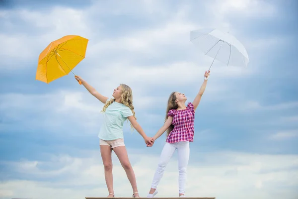 Listo para cualquier clima. Viento o lluvioso estamos preparados. Libertad y frescura. Pronóstico del tiempo. Cambio de clima. Niños despreocupados al aire libre. Chicas amigas con paraguas cielo nublado fondo — Foto de Stock