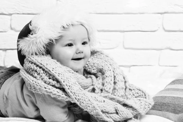 Piccolo bambino con adorabile viso curioso in maglione giallo posa sulla pancia in cappello di Capodanno e sciarpa lavorata a maglia sul retro della parete di mattoni bianchi — Foto Stock