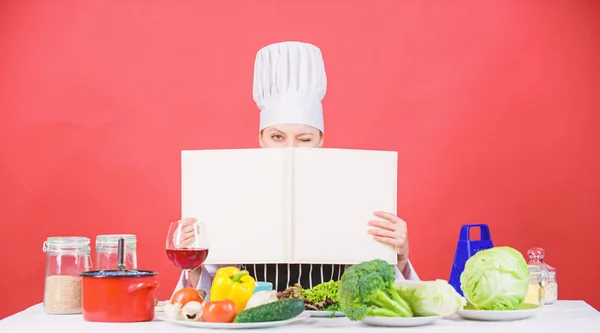 She is a super cook. Lady cook looking for cooking recipe in cookbook. Pretty woman reading cook book in kitchen. Cute cook housekeeper at kitchen table, copy space