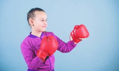 Klişenin aksine. Boks eldivenli boksör çocuk. Kendine güvenen bir genç. Spordan zevk. Kadın boksör. Spor terbiyesi. Boks sıkı disiplin sağlar. Mavi arka plan üzerinde kız sevimli boksör