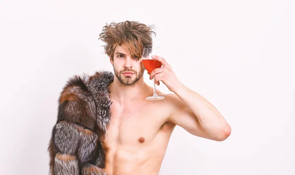 Estilo de vida y bienestar de lujo. Riqueza y concepto de lujo. Chico atractivo posando abrigo de piel en cuerpo desnudo. Símbolo de lujo. Sexy somnoliento macho tousled pelo beber vino o alcohol aislado en blanco — Foto de Stock