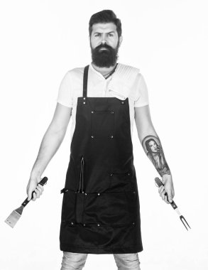 Hizmet Barbekü. Barbekü Izgara araçlarını elinde olan sakallı adam. Hipster önlük Barbekü için metal mutfak eşyaları ile ızgara. Izgara aşçı. Kullanarak bir barbekü ızgara gıda hazırlama ayarla