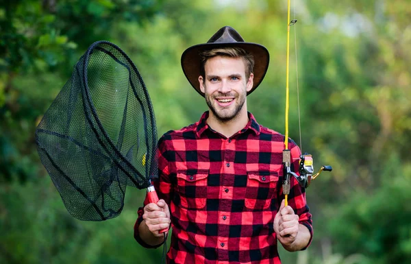 趣味で釣りをする釣り道具の自然の背景を持つチェッカーシャツのハンサムな男。夏の週末のコンセプト。ロッドスピニングネットを持つヒップスター漁師。素敵な釣りを願っています。釣りの日 — ストック写真