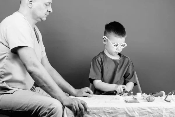Illness treatment. Dad and son medical dynasty. Medical examination. Boy cute child and his father doctor. Hospital worker. Health care. Medicine concept. Kid little doctor sit table medical tools