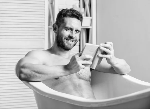 Sexy Mann im Badezimmer lesen. Macho nackt in Badewanne. Sex und Entspannungskonzept. Der Mensch hat einen muskulösen Körper. Schaum vorsichtig mit Wasser abwaschen. Bücherliebhaber. Macho genießt Buch im Bad. glücklicher Mann — Stockfoto