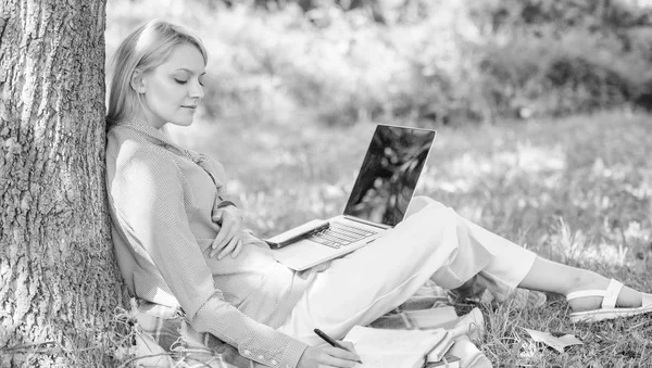 Tecnología educativa y concepto de internet. Chica trabajar con el ordenador portátil en el parque sentarse en la hierba. Oficina de medio ambiente natural. Beneficios de trabajo al aire libre. Mujer con ordenador portátil de trabajo al aire libre se apoyan en el tronco del árbol —  Fotos de Stock