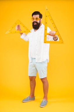 Çiziminiz için ihtiyacınız olan araçlar. Geometri veya teknik çizim öğretmeni. Sakallı adam sarı arka planda çizim aletleri tutuyor. Mühendislik çizimi yapmak için üçgen kullanan mühendis