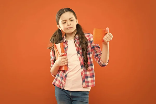 Esta no es mi taza de té. Chica insatisfecha mirando taza durante el almuerzo sobre fondo naranja. Niño en edad escolar almorzando. Niña en el almuerzo escolar. Niño bebiendo té o leche para el almuerzo — Foto de Stock