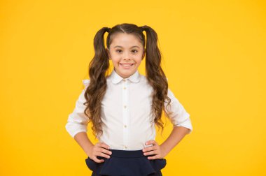 Okula hoş geldin. Sevimli gülümsemeile küçük bir okul çocuk. Küçük bir okul çocuğu sarı arka planda gülümsüyor. Mutlu küçük kız okula dönüyor. Resmi giyim uzun esmer saçlı sevimli küçük çocuk