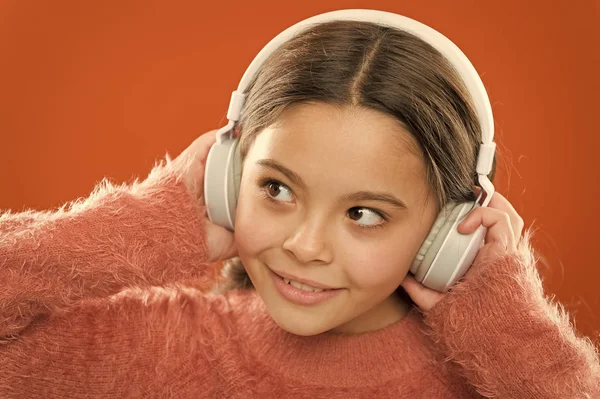 Niña linda niña usar auriculares escuchar música. Niño escuchar música fondo naranja. Música recomendada basada en el interés inicial. La forma más fácil de encontrar nueva música similar a las canciones que ya amas —  Fotos de Stock