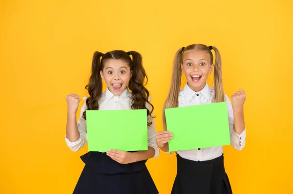 Huiswerk gedaan. Gelukkige kleine kinderen houden lege huiswerk bladen op gele achtergrond. Schattige kleine meisjes glimlachen met lege groene school posters voor huiswerk toewijzing. Huiswerk, kopieer ruimte — Stockfoto