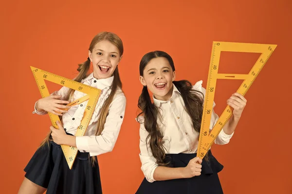 Estudiantes de escuela aprendiendo geometría. Uniforme escolar para niños sobre fondo naranja. Alumnos chicas lindas con grandes gobernantes. Geometría asignatura escolar. Dibujo con pizarra de regla. Educación y concepto escolar —  Fotos de Stock