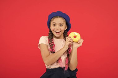Kız tatlı çörek elinde kırmızı camlı arka plan tutun. Çocuk gülümseyen kız donut yemeye hazır. Şeker dükkanı ve ekmek kavramı. Pişmiş Donuts büyük fanlar çocuklar. Resist taze yapılmış çörek imkansız