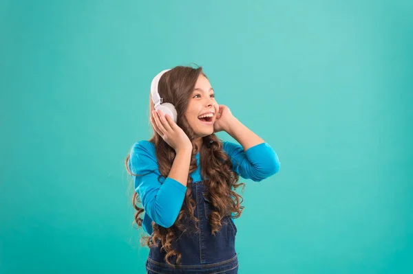 La música suena mejor con mis auriculares. Niña usando auriculares sobre fondo azul. Lindo niño escuchando música en auriculares estéreo para oídos. Adorable niño pequeño con auriculares modernos — Foto de Stock